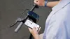 A person is holding a smartphone and looking at the screen while standing next to an electric scooter. Produktbild-Vorschau