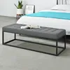 A gray upholstered bench with a metal frame sits in front of a bed with a blue throw blanket. Anteprima dell’immagine prodotto