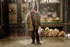 A man stands in the rain in front of a market with firewood stacked outside. Náhled obrázku produktu