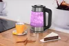 A glass electric kettle with purple light is shown on a wooden countertop next to a cup of tea, a slice of cake, and cinnamon sticks. Náhled obrázku produktu