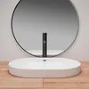 A white oval sink with a black faucet in front of a large round mirror. Produktbild-Vorschau