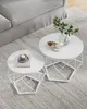 Two white coffee tables with geometric bases are on a gray rug next to a gray sofa. Náhled obrázku produktu