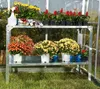 A metal plant stand with various potted flowers inside a greenhouse. Náhľad obrázku produktu