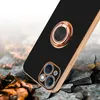 A black phone case with a gold ring holder and camera protection is shown on a cracked, rocky surface with fallen leaves. Produktbild-Vorschau