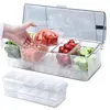 A hand is shown placing a clear container filled with sliced tomatoes into a larger clear container filled with ice. The larger container holds multiple smaller clear containers filled with various chopped vegetables and fruits, including lettuce, carrots, Produktbild-Vorschau