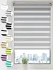 A window with a grey and white striped roller blind, with a city skyline visible through the window. Produktbild-Vorschau