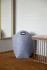 A grey felt laundry basket with brown handles sits on a wooden floor next to a small table with a brown top. Produktbild-Vorschau