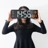 A person holds a digital clock in front of their face against a white background. Náhled obrázku produktu