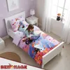 A young girl is lying on a bed with Frozen-themed bedding and reading a book. Produktbild-Vorschau