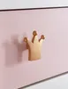 A close-up of a golden crown-shaped drawer pull on a pink dresser. Produktbild-Vorschau