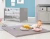 A baby is playing on a mat next to a crib. Náhled obrázku produktu