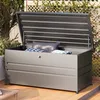 An open metal storage box on a wooden deck, filled with cushions, with greenery and a lattice fence in the background. Produktbild-Vorschau