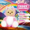 A teddy bear dressed as a unicorn sits in a colorful, whimsical landscape with a rainbow. Produktbild-Vorschau