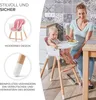 A mother feeding her baby in a high chair in a kitchen. Produktbild-Vorschau