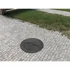 A black manhole cover is placed on a cobblestone path next to a patch of grass. Podgląd zdjęcia produktu