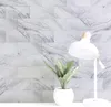 Weiße und graue Marmor-Aufklebefliesen an einer Wand, mit einer weißen Tischlampe und einer Topfpflanze auf einer weißen Fläche Produktbild-Vorschau