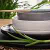 A close-up of stacked ceramic bowls and plates with chopsticks and green onions. Náhled obrázku produktu