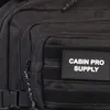 A close-up view of a black backpack with a patch that says "CABIN PRO SUPPLY". Náhled obrázku produktu