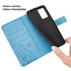 A hand is holding a black phone case over a blue wallet-style phone case with card slots and a floral design. Produktbild-Vorschau