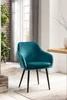 A teal velvet chair in a room with a wooden table and brick wall. Produktbild-Vorschau