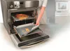A person is removing a baking sheet with food scraps from an oven, with a pizza on a rack inside the oven. Náhľad obrázku produktu
