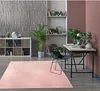 A modern living room or home office setup with a pink rug, a desk with a laptop, a chair, and shelving units. Produktbild-Vorschau
