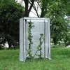 A small greenhouse with plants inside, set up on a grassy lawn with trees in the background. Produktbild-Vorschau