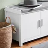A close-up view of a white shoe cabinet with a gray cushioned top, a woven basket with a striped cloth, and a gray hat on top of the cabinet. Náhľad obrázku produktu
