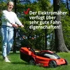 A woman is pushing an electric lawnmower on a grassy lawn with trees in the background. Produktbild-Vorschau