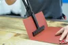 A person is using a tool to bend a piece of red material on a wooden surface. Voir les images du produit
