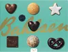 A collection of assorted festive baked goods and chocolates arranged on a teal background with gold lettering. Náhled obrázku produktu