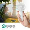 A woman in a yellow dress and white hat is enjoying the breeze from a white handheld fan held by someone. The background is sunny and outdoors. Produktbild-Vorschau