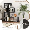 A black, multi-tiered, S-shaped bookshelf filled with books and decorative items, placed in a room setting next to a large potted plant. Podgląd zdjęcia produktu