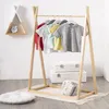 A wooden children's clothing rack with several t-shirts hanging on it, placed on a wooden floor with a rug and a decorative shelf in the background. Náhled obrázku produktu