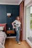 A woman stands in a bedroom holding a foldable step stool near a window. Podgląd zdjęcia produktu