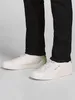 A person wearing black pants and white sneakers. Voir les images du produit