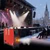 A red diesel heater is shown in the foreground, emitting smoke, with a band performing on a stage in the background during a snowy outdoor concert. Náhled obrázku produktu