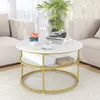 A round coffee table with a marble-like top and gold metal legs, placed in a living room setting with sofas and a plant. Produktbild-Vorschau