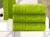 Three green towels are stacked on a white surface, with a sink and decorative reeds in the background. Náhľad obrázku produktu