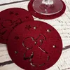Several red felt coasters with cut-out angel and star designs are arranged on a light-colored wooden surface. A wine glass is placed on one of the coasters. Produktbild-Vorschau