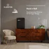A retro-style black mini-fridge is placed on a wooden dresser next to a cream armchair and a floor lamp. Produktbild-Vorschau