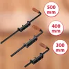 Three spring-loaded bolts with wooden handles are displayed diagonally against a blurred brown and orange background. Circular labels with measurements are placed to the right of the bolts. Náhled obrázku produktu