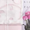 A close-up view of a sheer white curtain with a pink floral pattern, layered over a pink surface. A bouquet of pink roses is visible on the right side. Produktbild-Vorschau