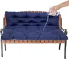 A hand is pouring water from a glass onto a dark blue bench cushion, demonstrating its water-repellent feature. Produktbild-Vorschau