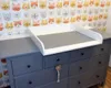 A white changing tray sits on top of a gray dresser with a cat-themed wallpaper in the background. Podgląd zdjęcia produktu