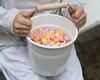 A child's hands hold a white bucket filled with colorful candies. Produktbild-Vorschau