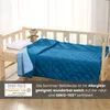 A blue quilted blanket on a child's bed with a teddy bear and pillow. Produktbild-Vorschau