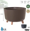 A product image showcasing a brown planter with wooden legs, along with icons and text indicating its features and eco-friendliness. Smaller images of a dark gray planter and a saucer are also present. Náhľad obrázku produktu