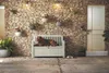 A dog rests on a white storage bench in front of a stone wall with hanging plants. Náhľad obrázku produktu