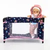 A doll is standing in a playpen with a floral pattern. Produktbild-Vorschau